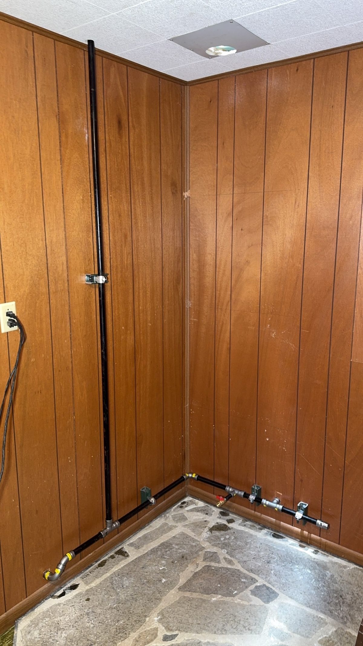 Indoor black iron gas pipe installation running along wall with baseboard connections